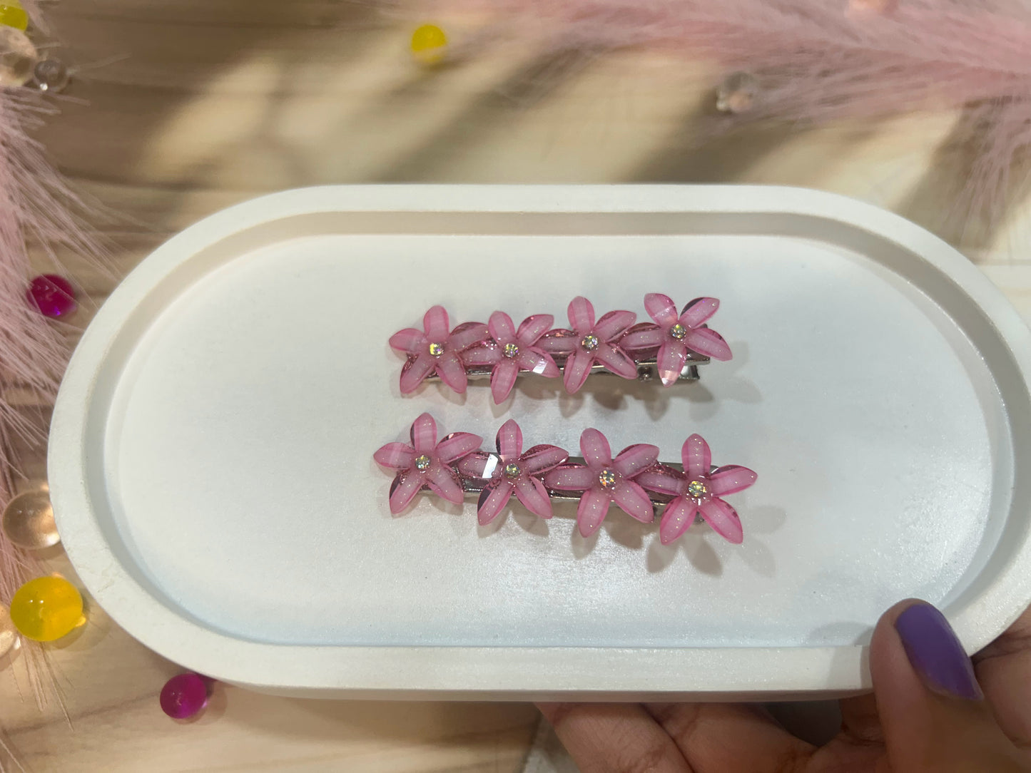 Pink floral hair clips on a white tray held by a hand with purple nail polish.