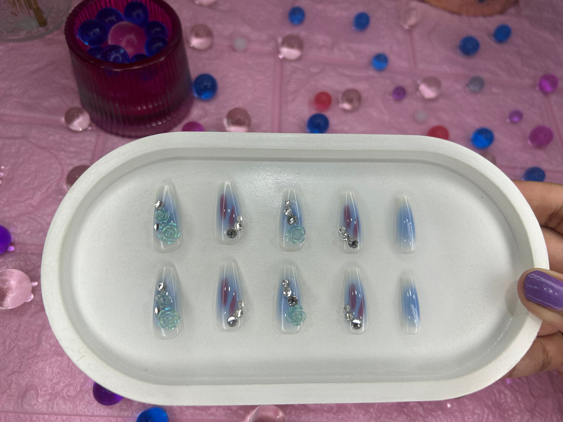 Set of false nails in a white tray on a pink surface with colorful confetti.