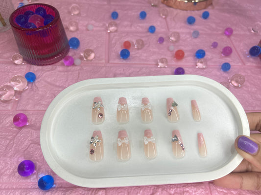 Set of decorative false nails on a white tray with a pink background and scattered decorative items.