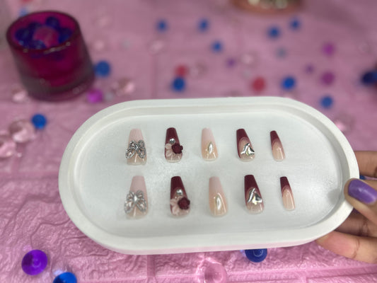 Set of nail art designs in a white case on a pink surface with colorful beads.