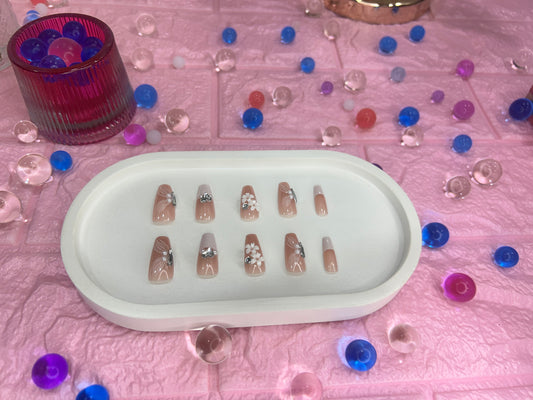 Set of false nails on a white tray with decorative beads on a pink surface