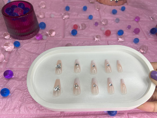 Set of false nails in a white tray on a pink surface with colorful beads.