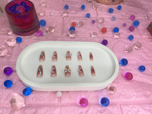 Set of false nails in a white tray with colorful beads on a pink surface