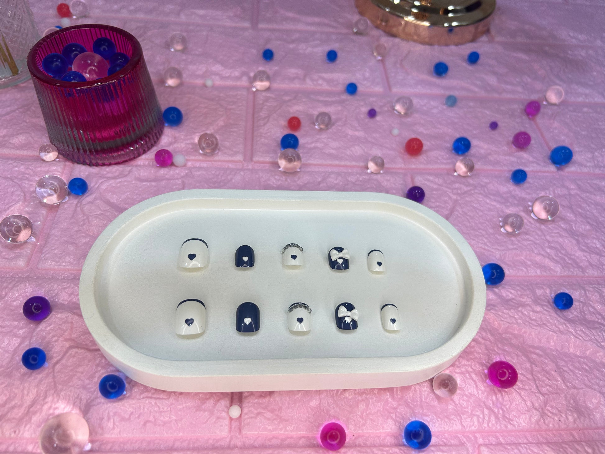 Set of nail art in a white dish with colorful beads scattered around on a pink surface