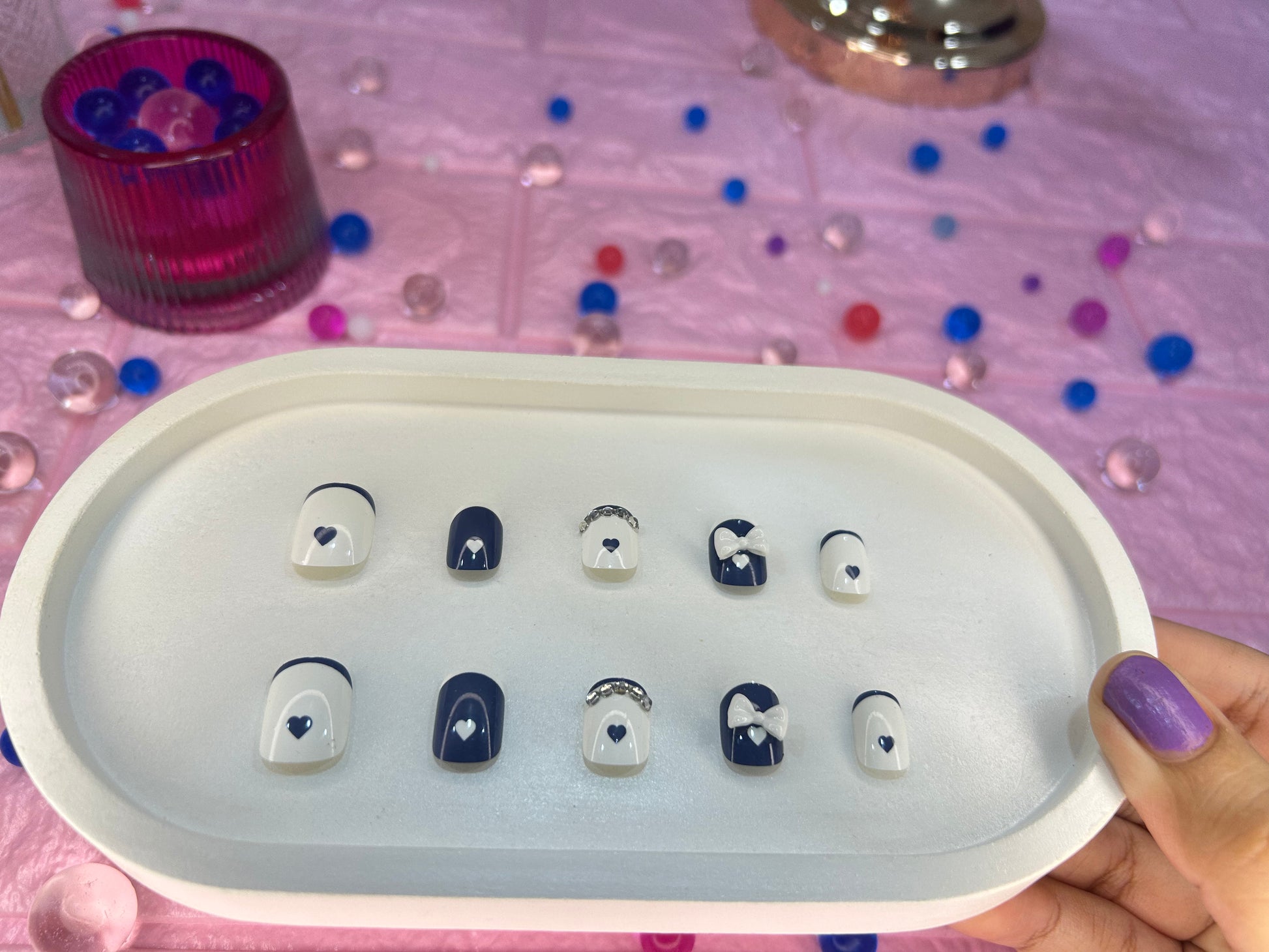 Set of small decorative items on a white tray held by a hand with purple nail polish.
