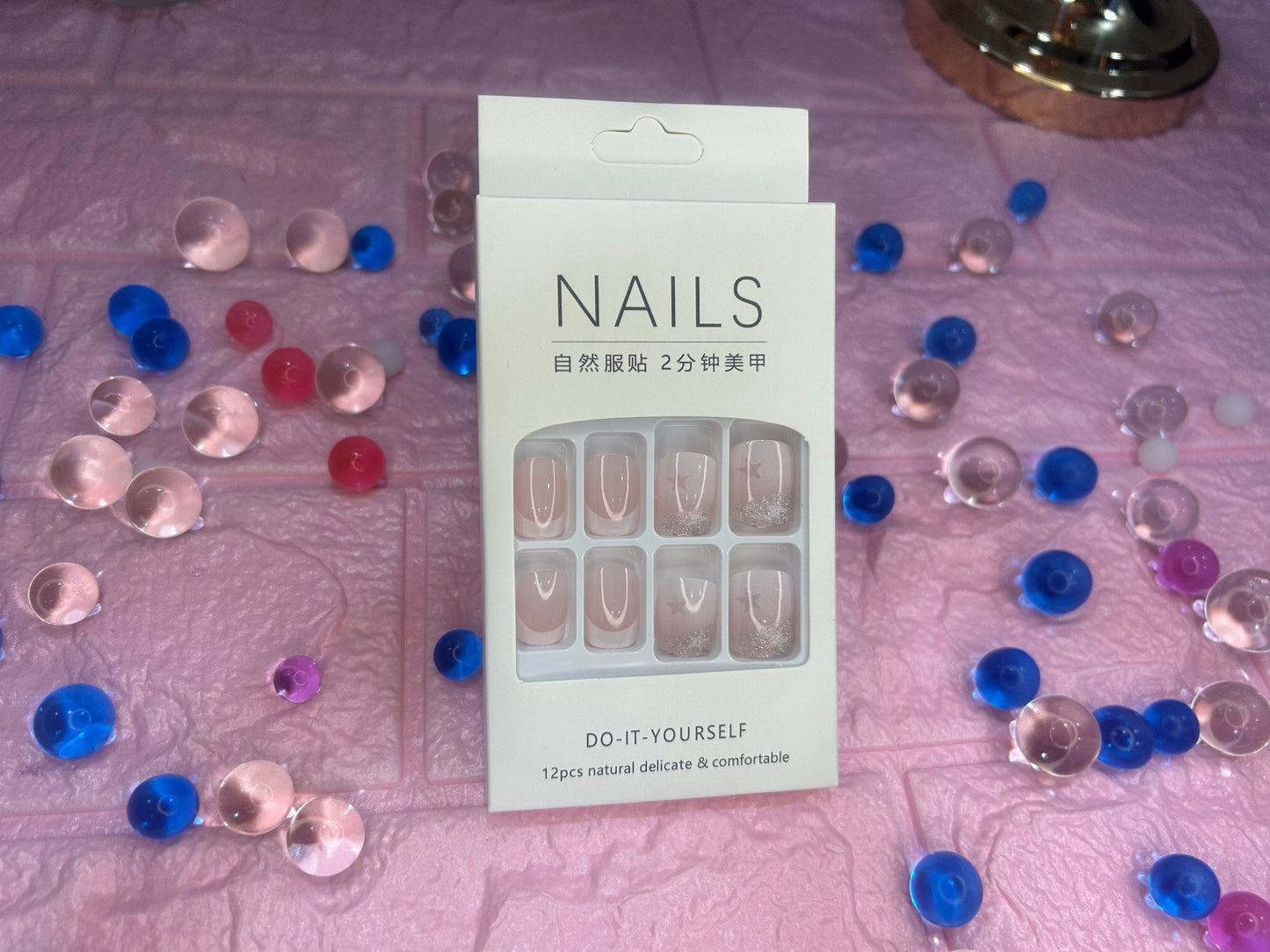 Packaging of 'Nails' product with decorative items on a textured surface