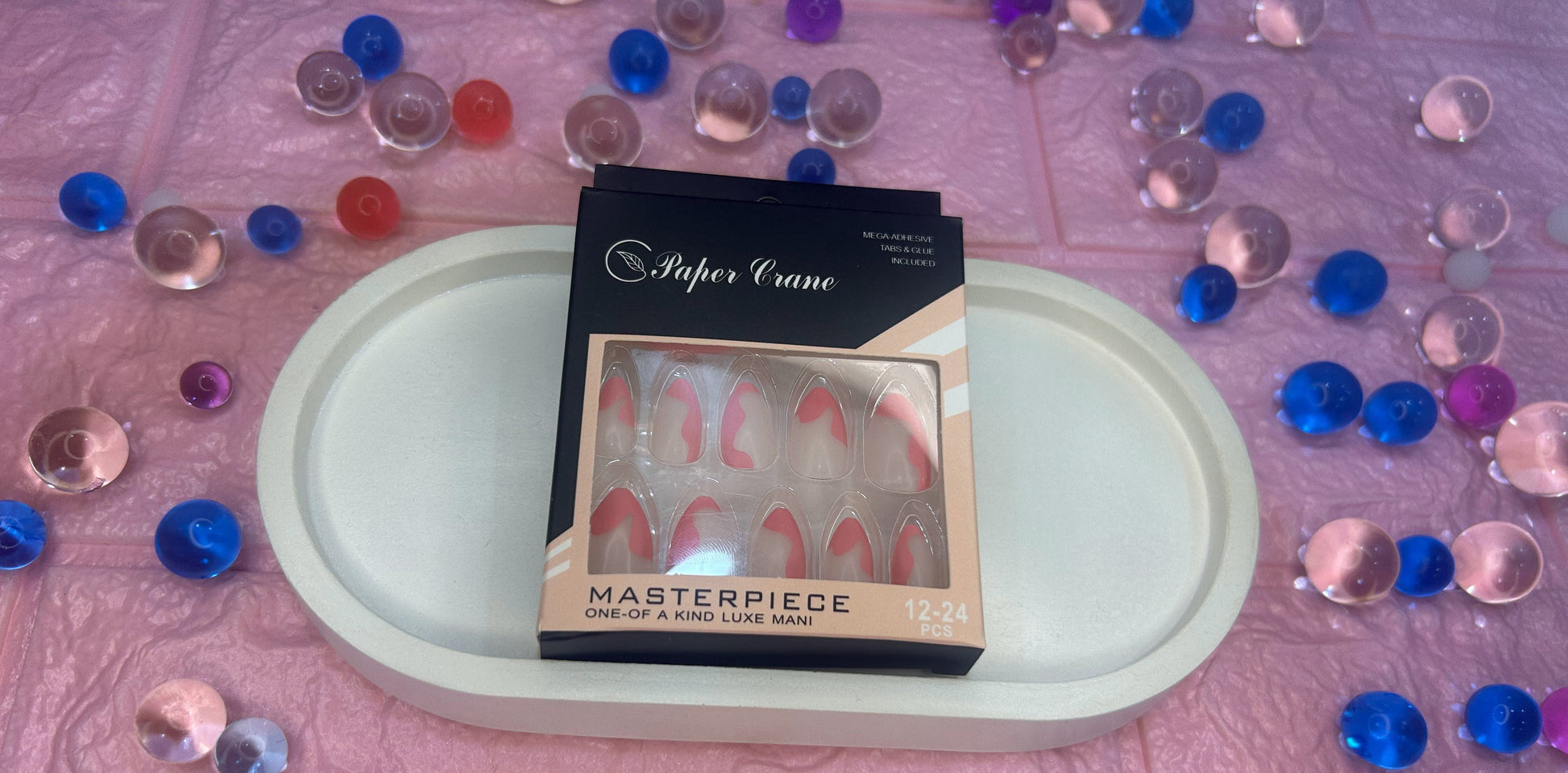 Nail art set packaging on a tray with decorative stones on a pink textured background