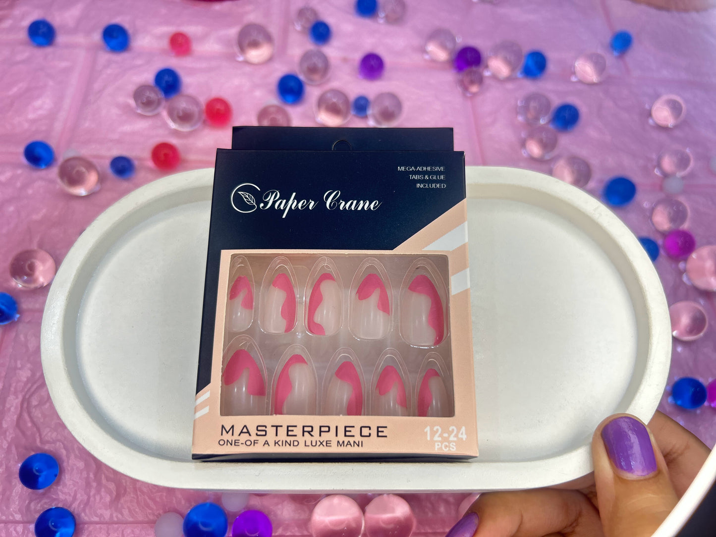 Packaged false nails with 'Paper Crane' branding on a pink surface with decorative stones.