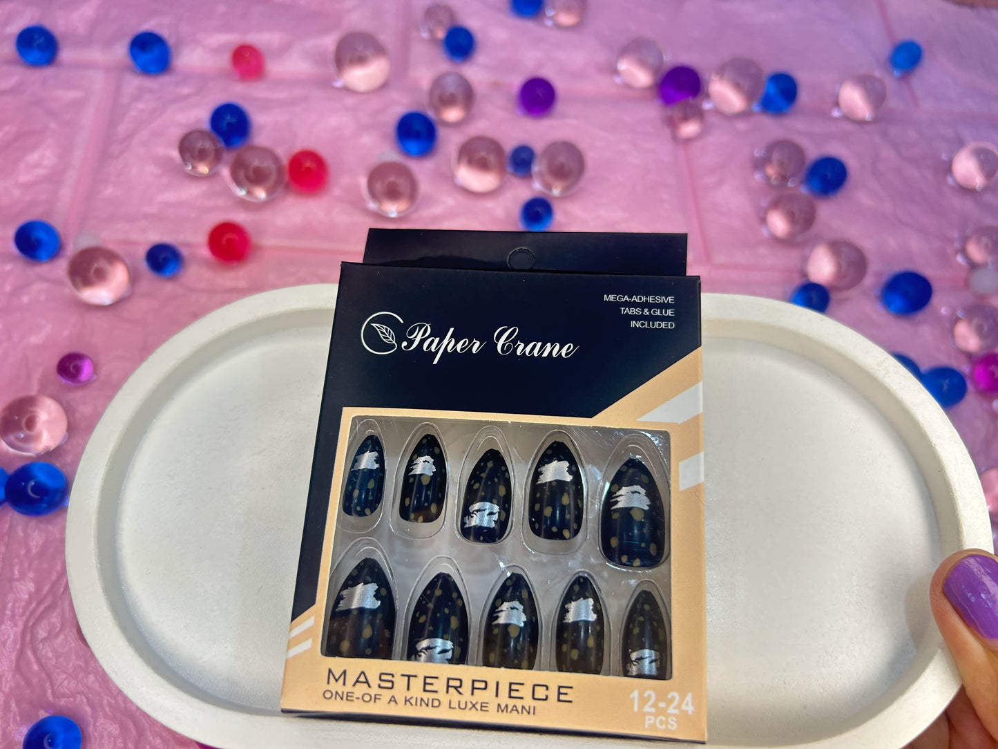 Packaged nail art with 'Paper Crane' branding on a pink surface with colorful beads.