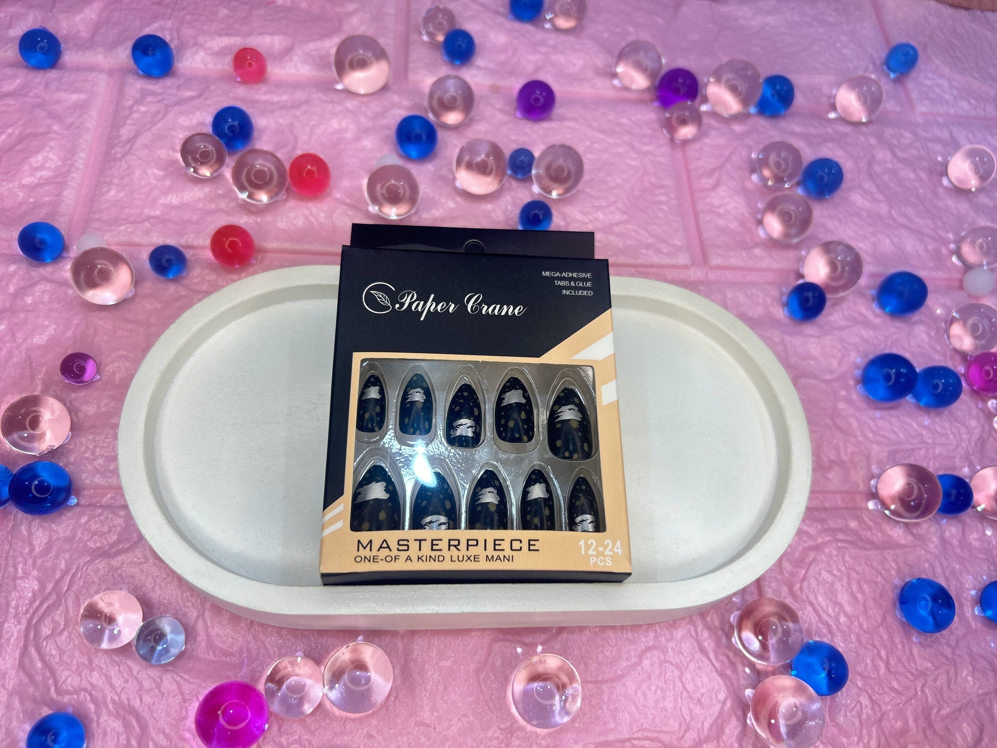 Box of false nails with 'Paper Crane' branding on a pink surface with decorative stones.