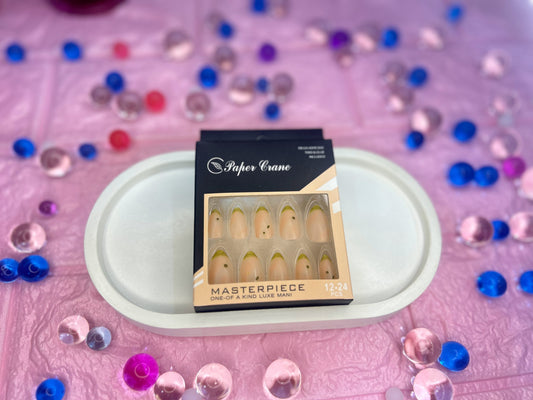 Box of false nails with 'Paper Crane' branding on a pink surface with decorative stones.