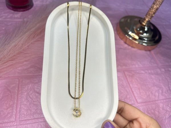 Gold necklace with a pendant on a white tray held by a hand against a pink textured background