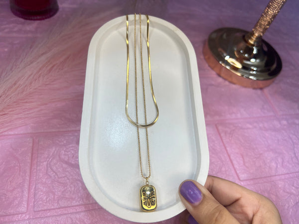 Gold necklace with a pendant on a white tray, held by a hand with purple nail polish.