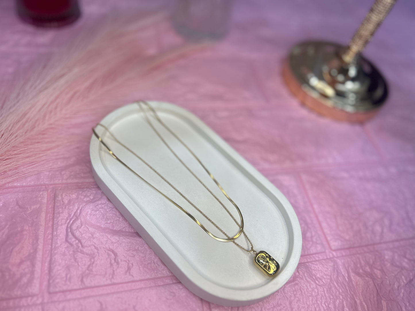 Gold necklace with pendant on a white stand against a pink textured background