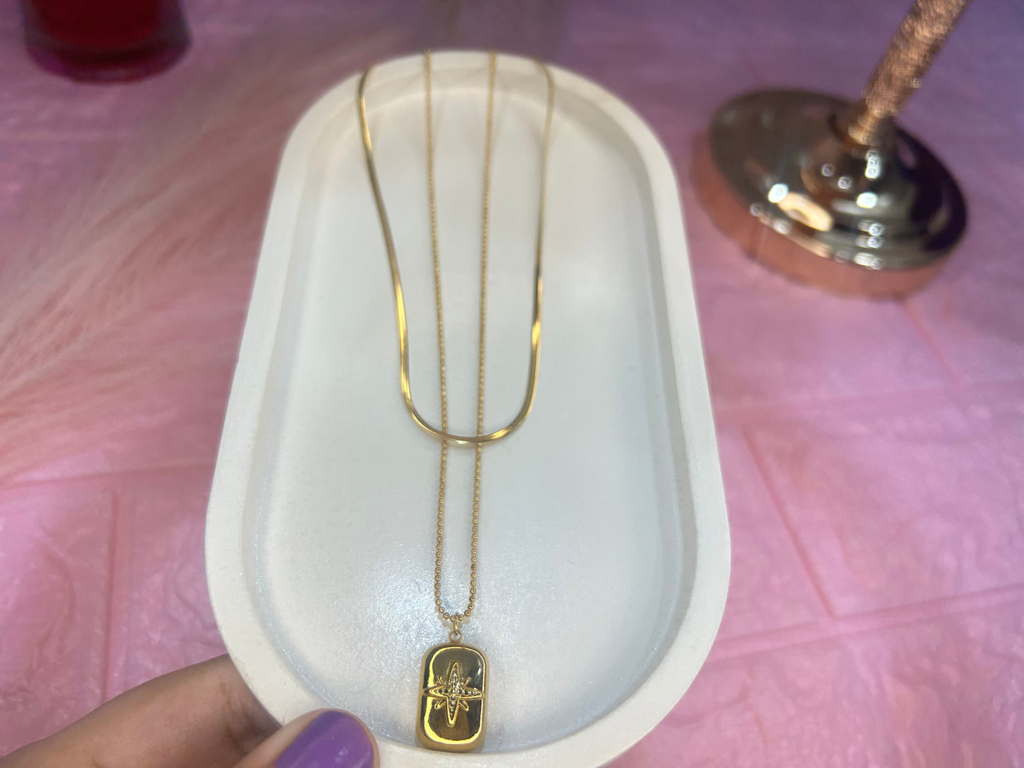 Gold necklace with a pendant on a white stand against a pink background
