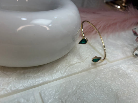 Gold earring with green gemstones on a textured surface