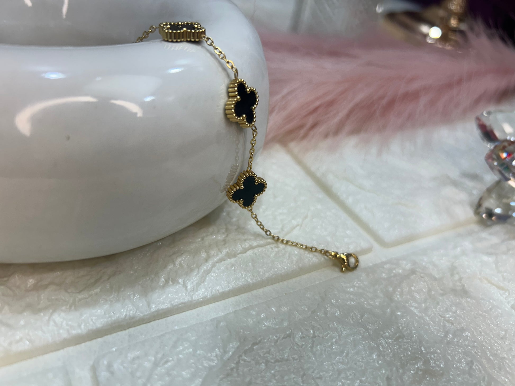 Gold bracelet with black clover charms on a white surface