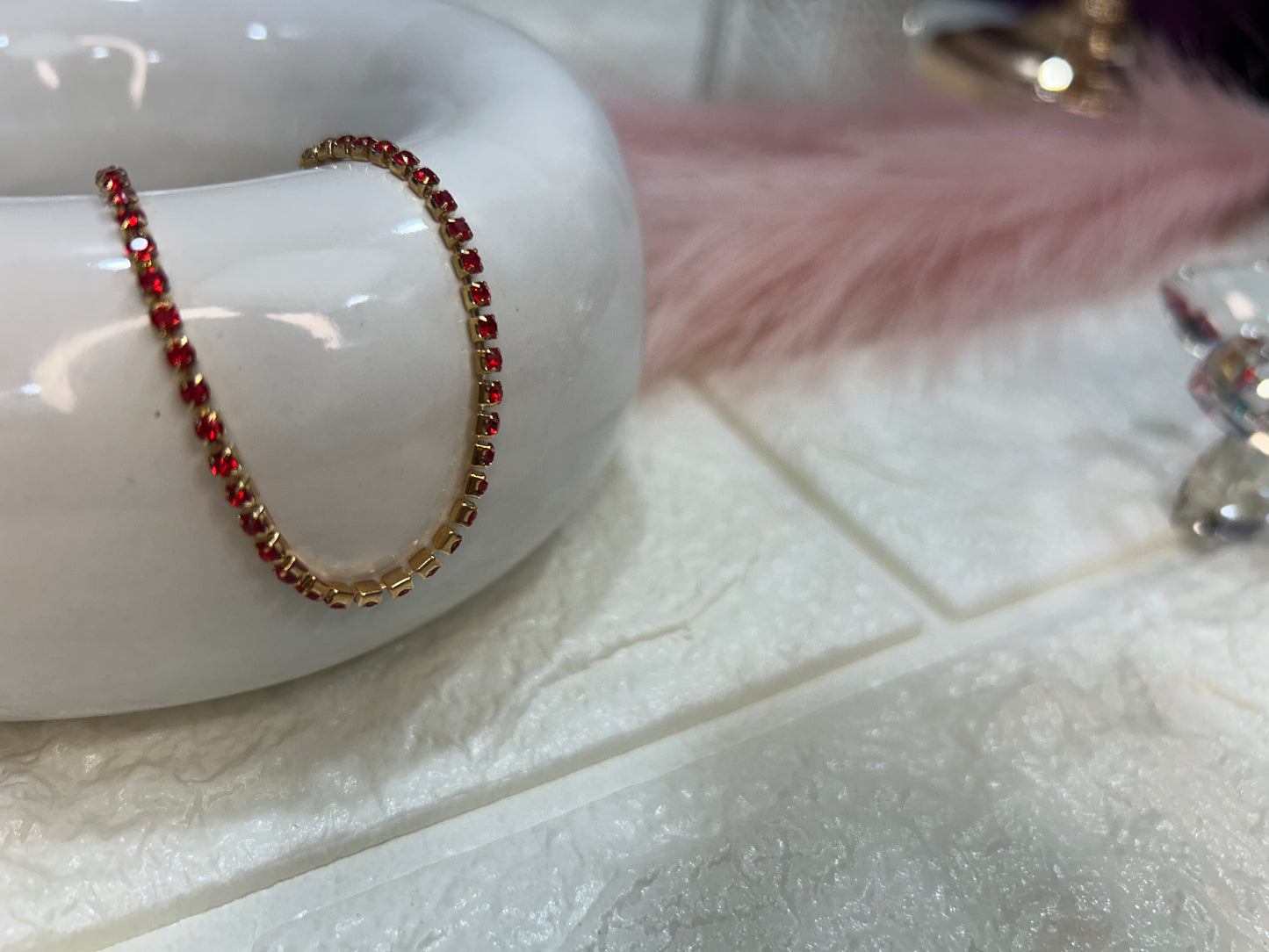 Bracelet with red beads on a white ceramic dish with a pink feather in the background.