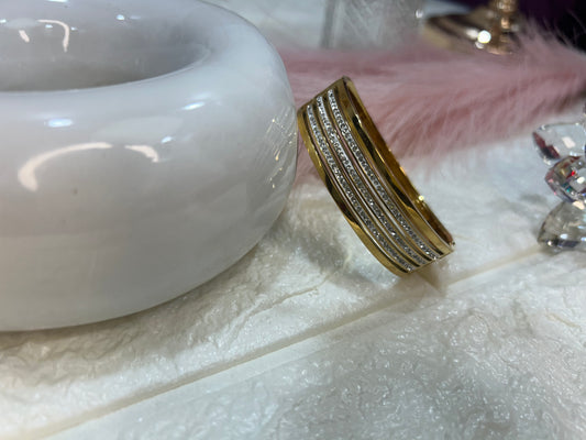 Gold bracelet on a textured white surface with a white ceramic object in the background