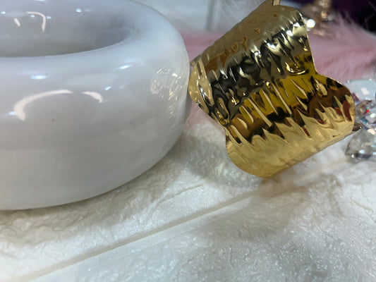 Gold ring with textured design next to a white ceramic bowl on a light surface.