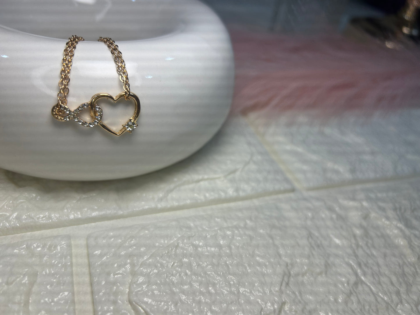 Gold necklace with heart-shaped pendant on a white ceramic dish.