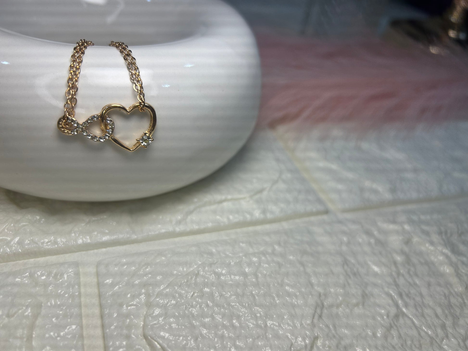 Gold necklace with heart-shaped pendant on a white ceramic dish.