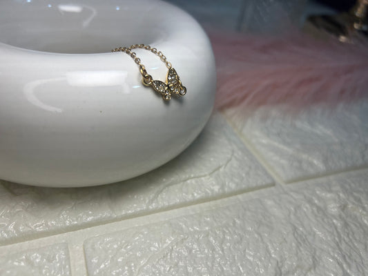 Gold butterfly necklace on a white surface with a blurred background
