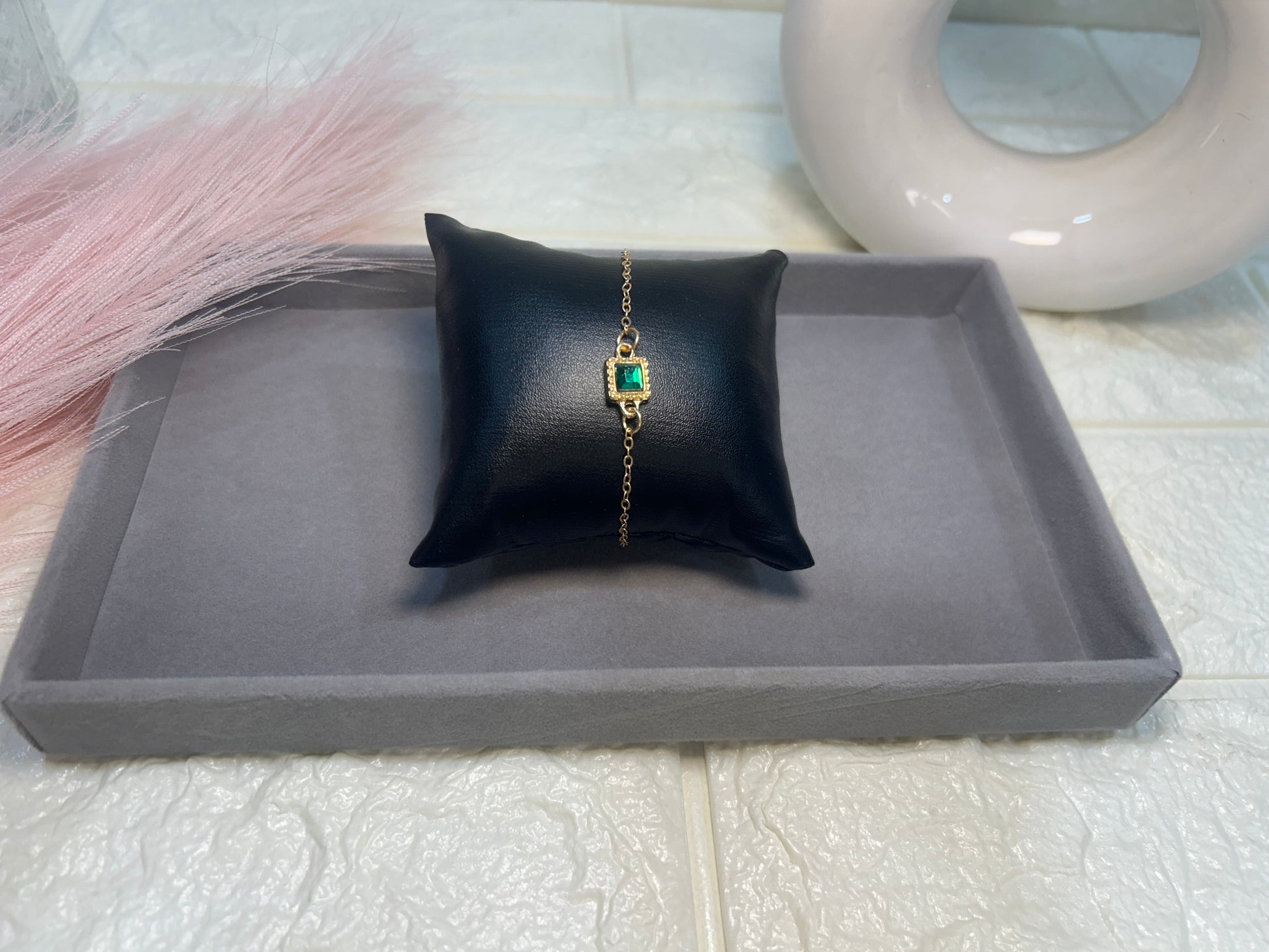 Jewelry bracelet with green gemstone on a black cushion on a gray tray.