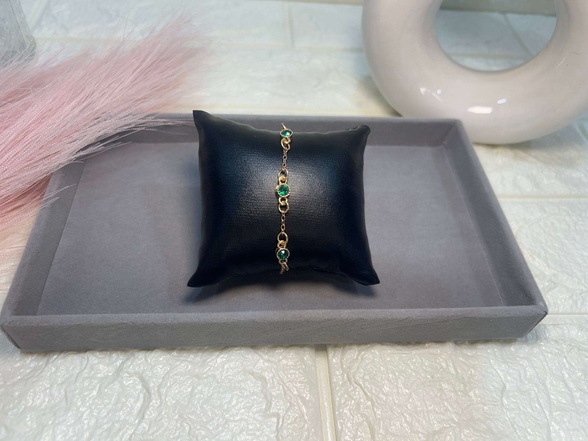 Bracelet with green stones on a black pillow on a gray tray