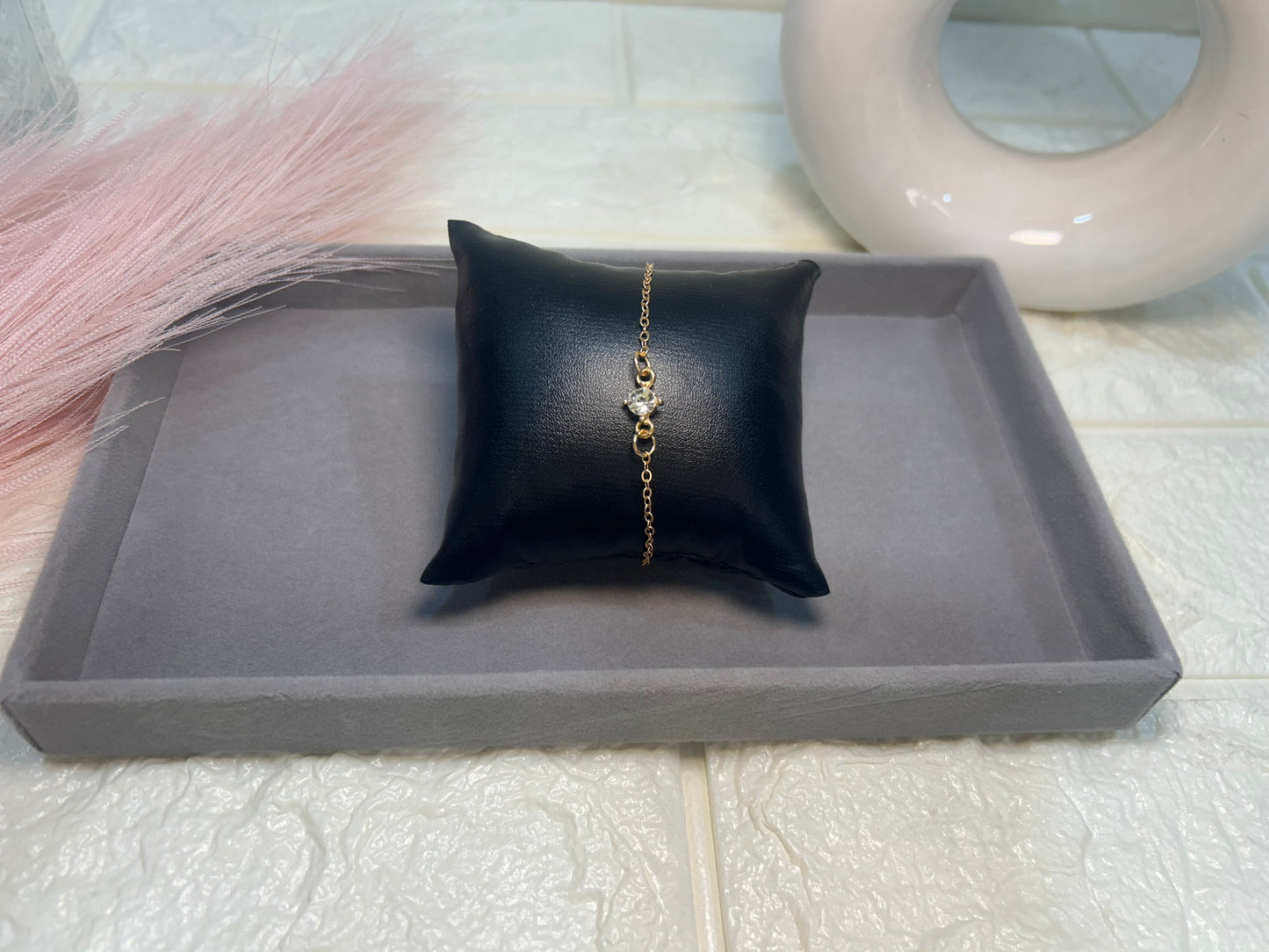 Gold bracelet on a black pillow on a gray tray with a white background