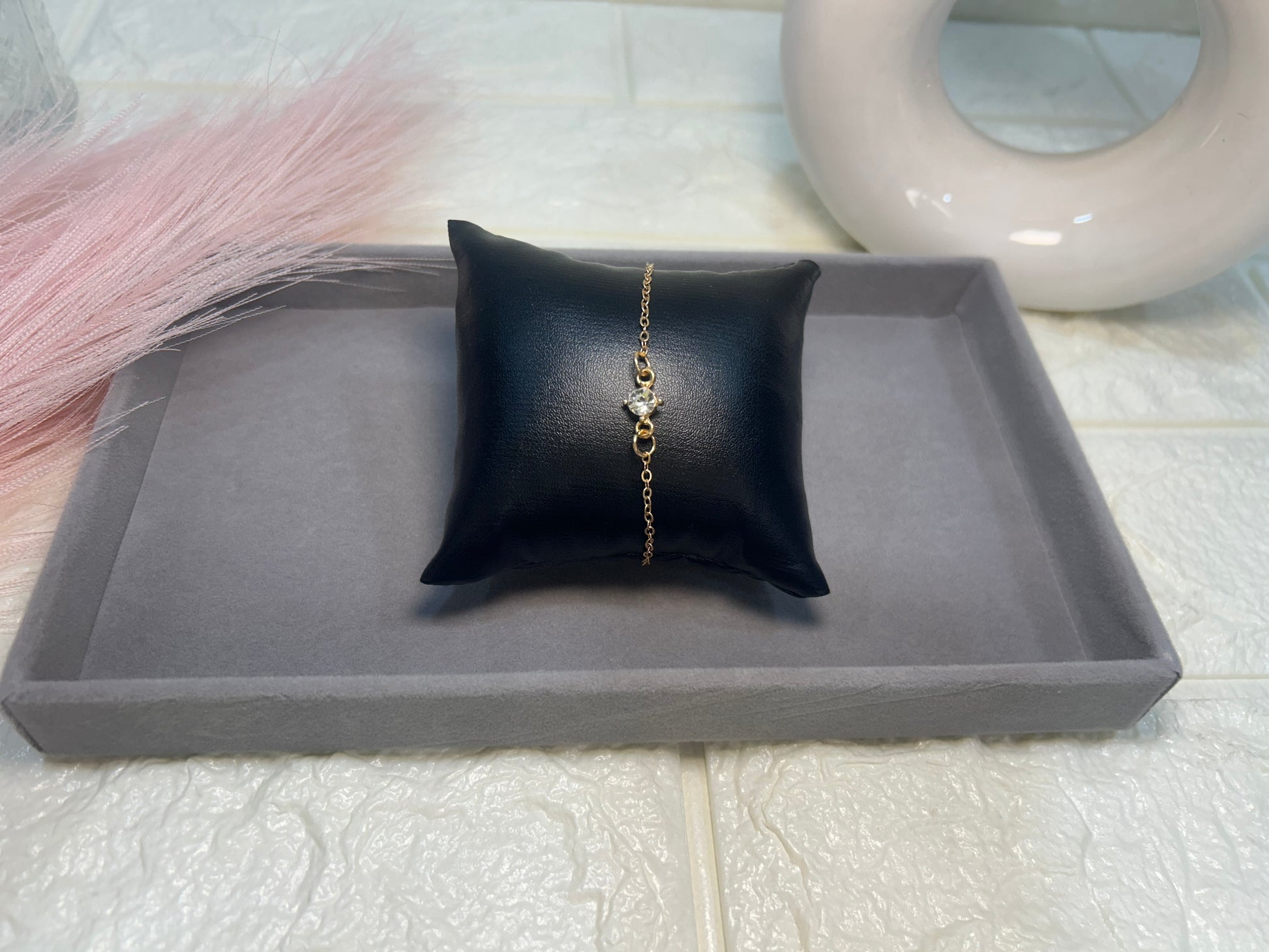 Gold bracelet on a black pillow on a gray tray with a white background