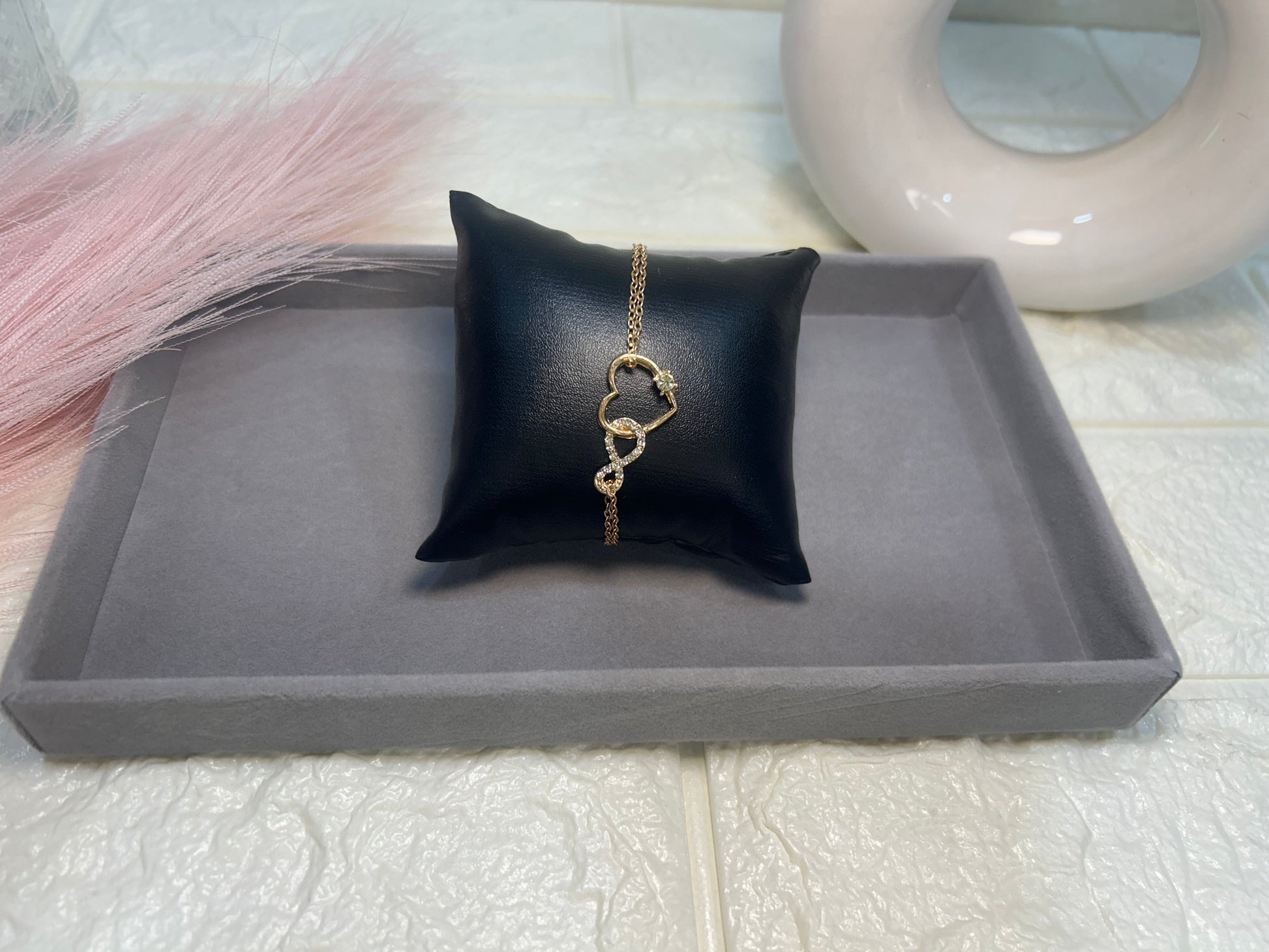 Gold necklace on a black pillow with a gray tray and pink fabric in the background