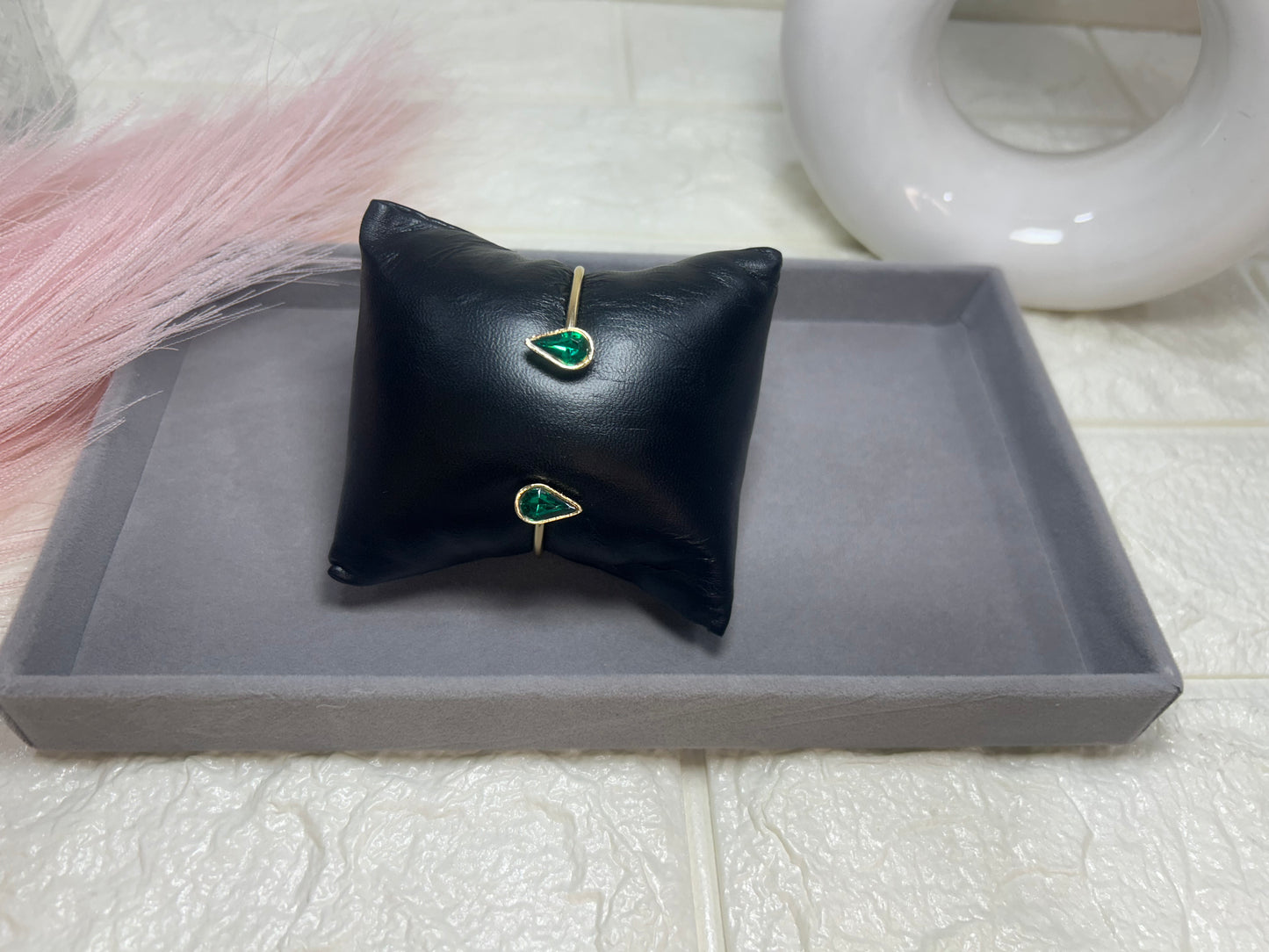 Black jewelry pillow with green gemstone earrings on a gray tray.