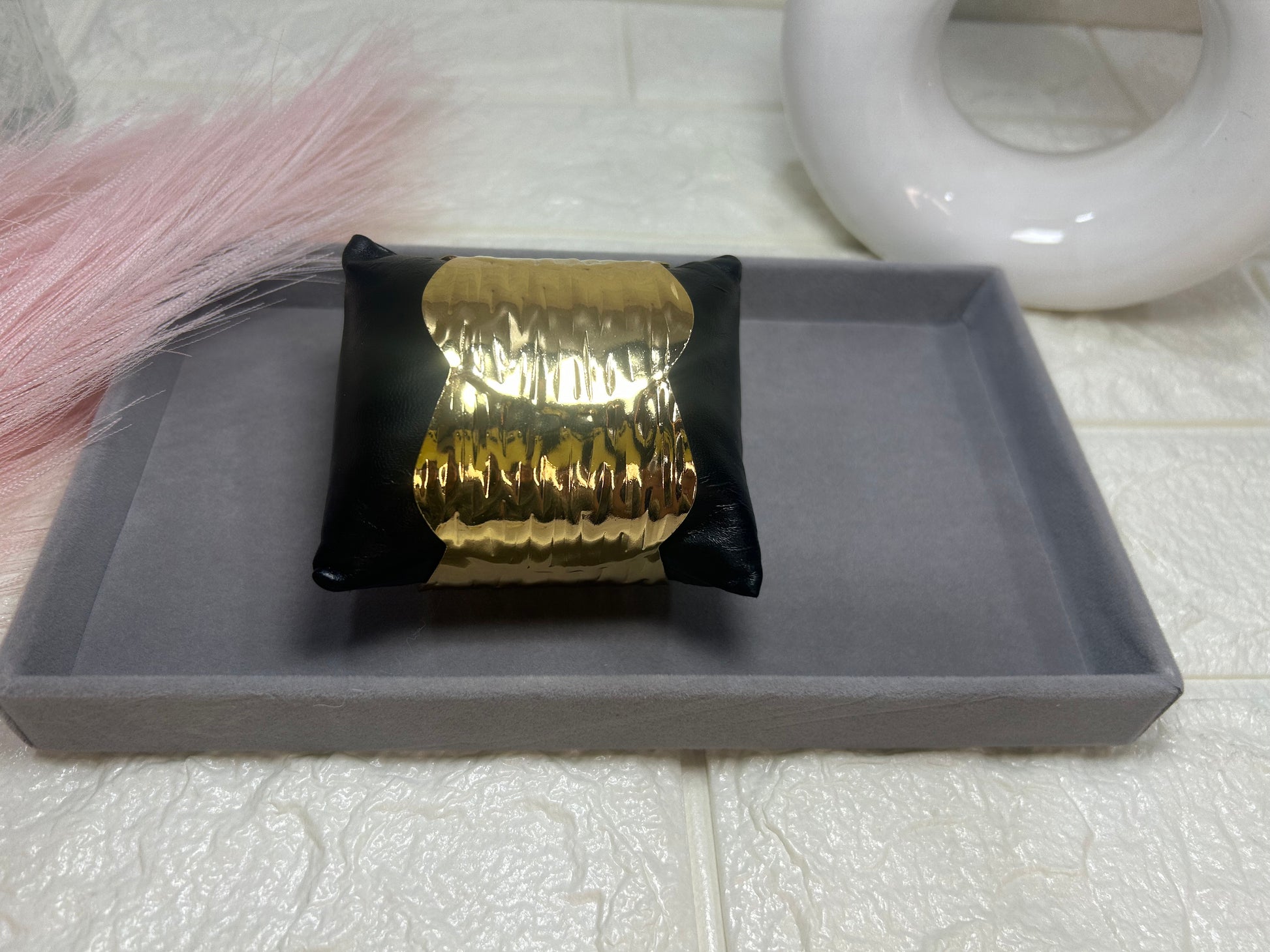 Gold bracelet on a black cushion with a gray tray underneath, on a tiled floor.