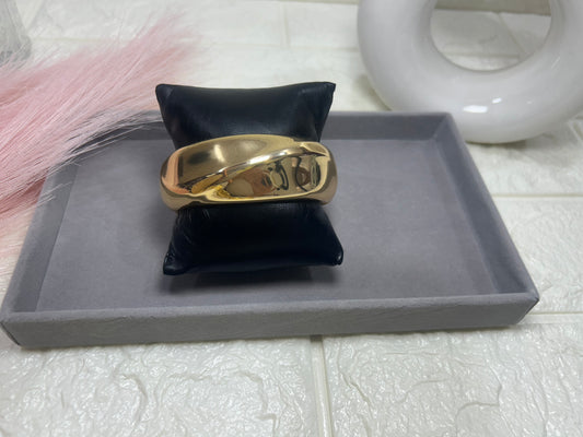 Gold ring on a black cushion with a gray tray and white vase in the background