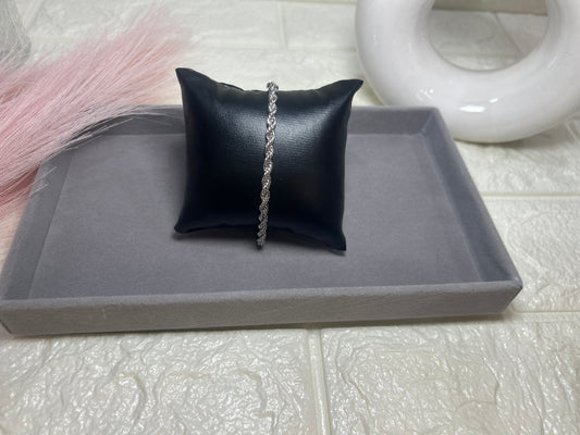 Black jewelry pillow with a silver chain on a gray tray against a tiled background
