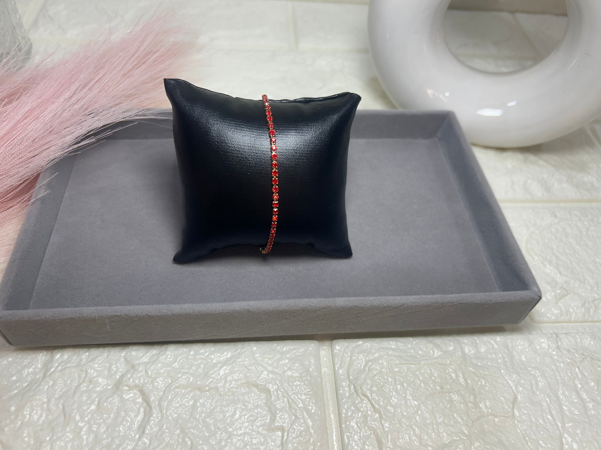 Bracelet with red beads on a black pillow on a gray tray with a white background