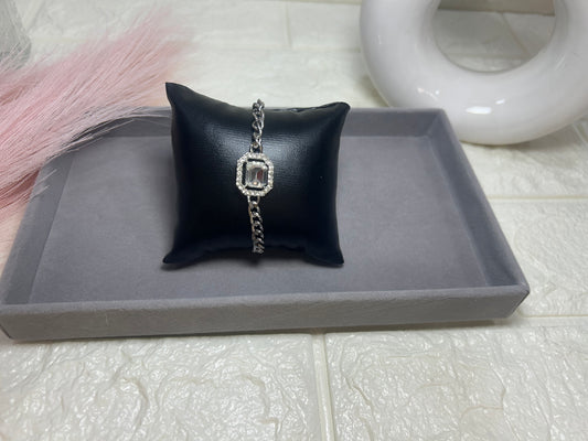 Silver bracelet on a black pillow with a gray tray underneath, on a tiled floor.
