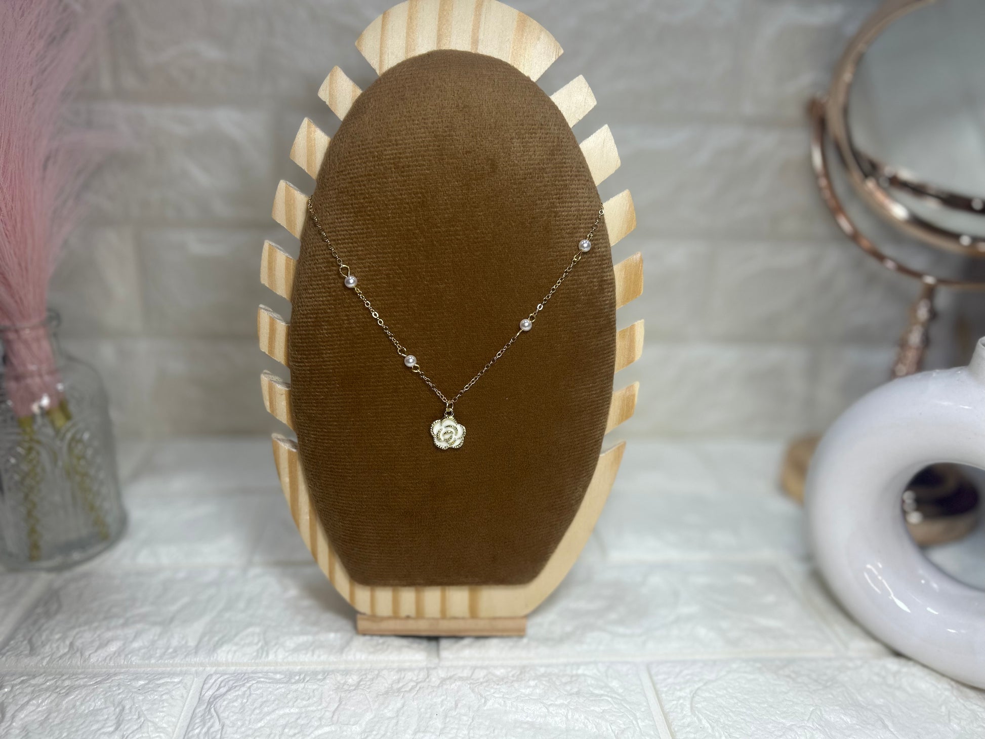Necklace on a brown velvet stand with a textured white surface and decorative items in the background.