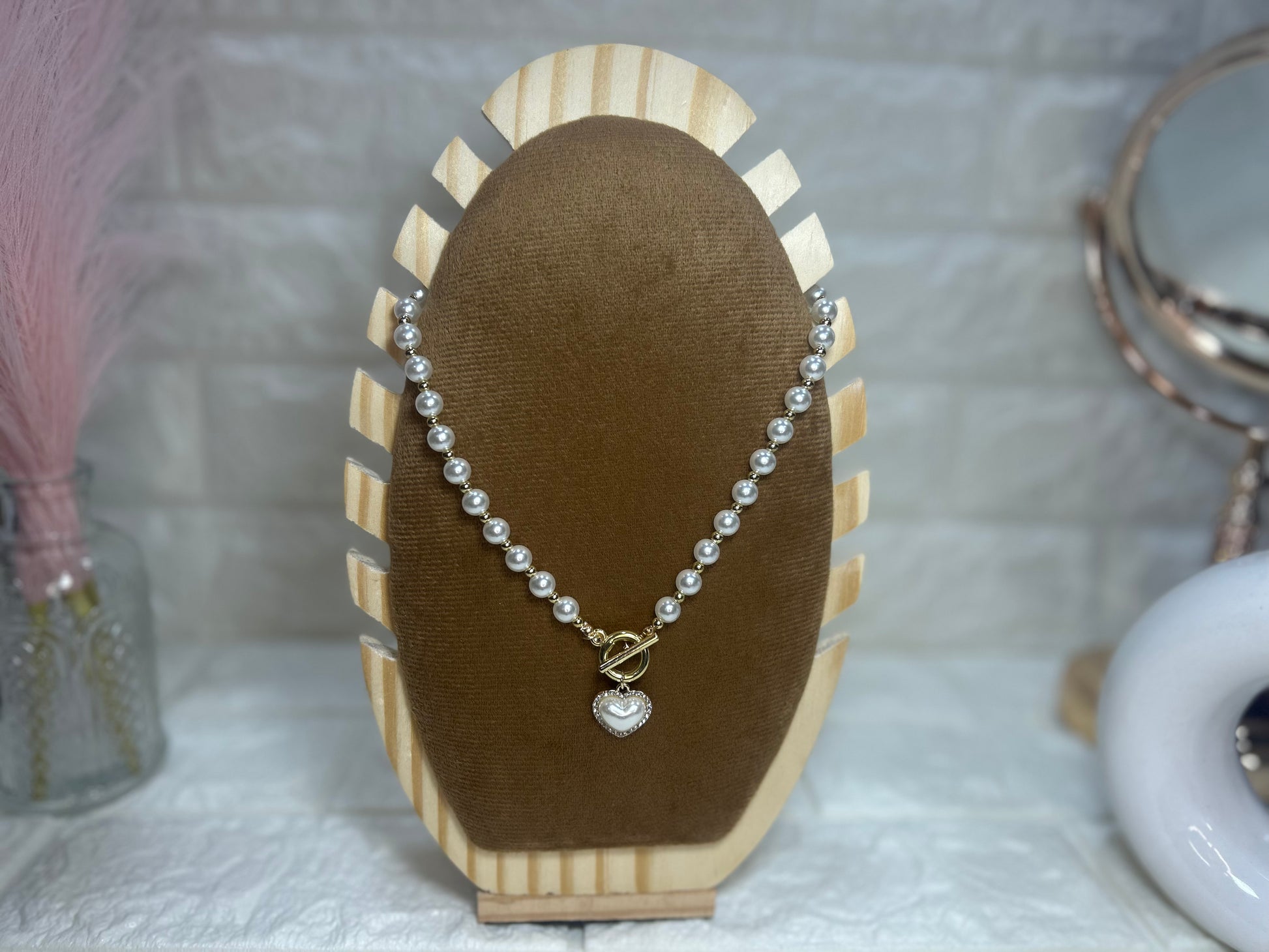 Pearl necklace with a heart charm on a brown jewelry display stand.