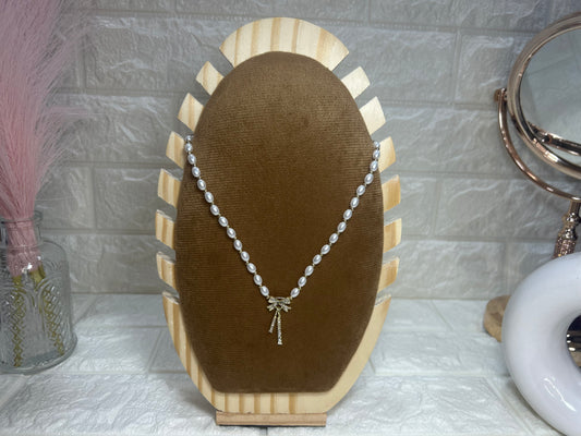 Pearl necklace on a brown velvet display stand with a decorative background.