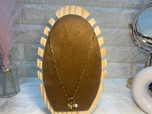 Gold chain necklace with a pendant on a wooden display stand against a textured wall.