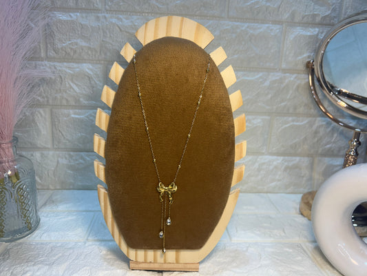 Necklace on a brown velvet cushion with a wooden stand against a textured wall.