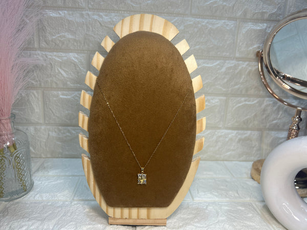 Necklace on a brown velvet stand with a marble-patterned wall in the background