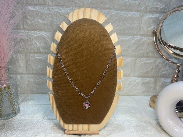 Necklace with a heart pendant on a wooden display stand against a textured wall.