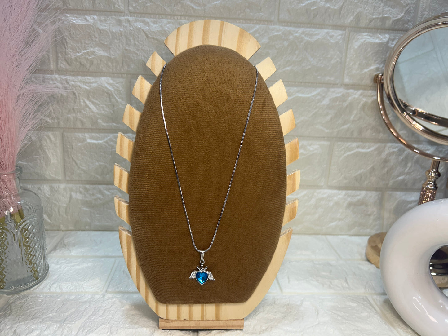 Necklace with a pendant on a wooden stand against a tiled wall.