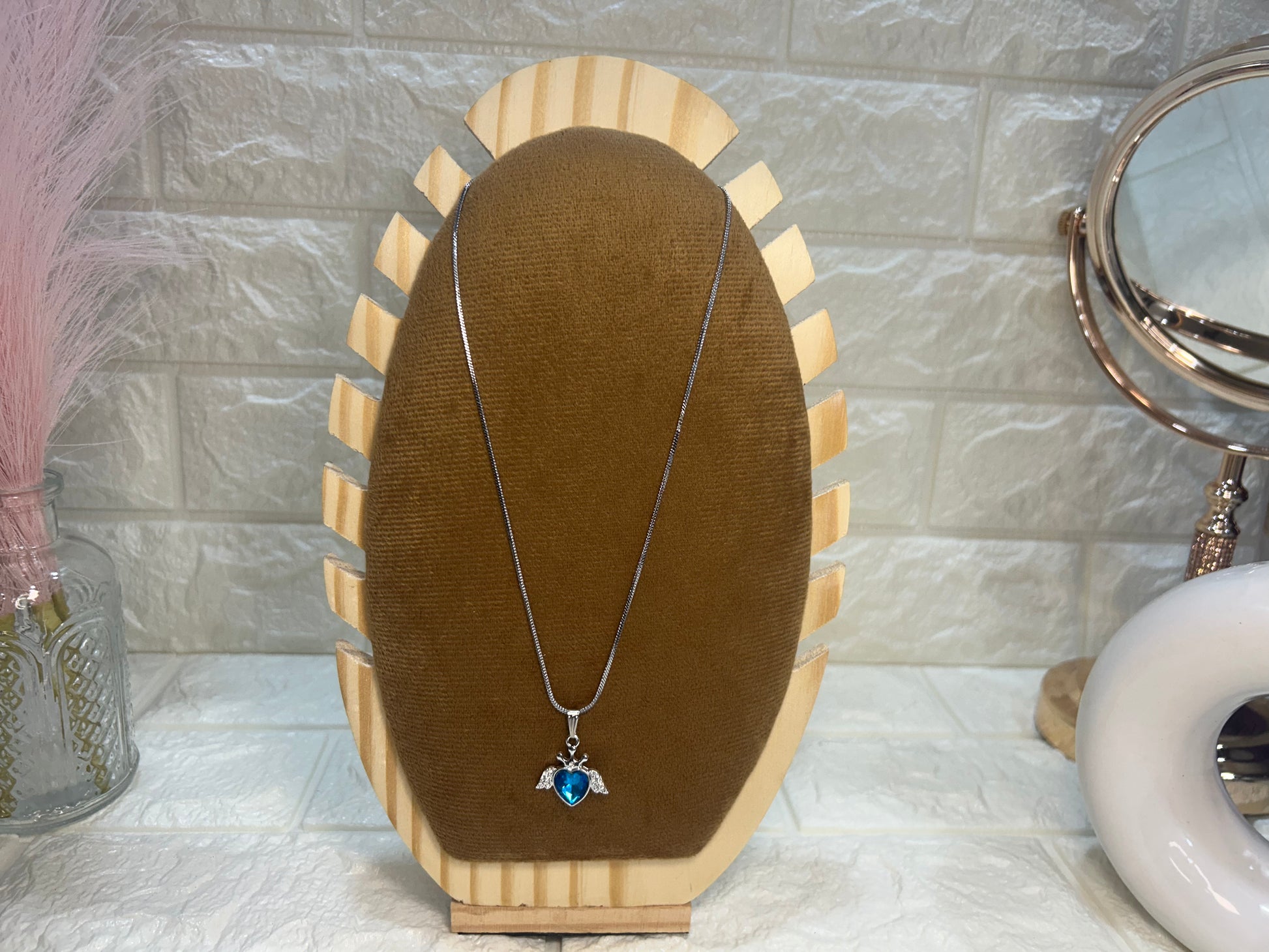 Necklace with a pendant on a wooden stand against a tiled wall.